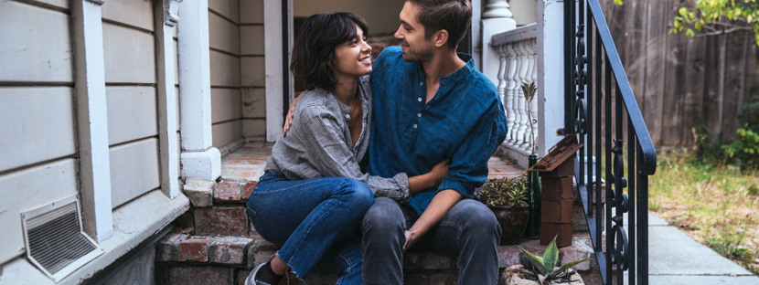 Two people happily hugging while sitting on their house's staircase.